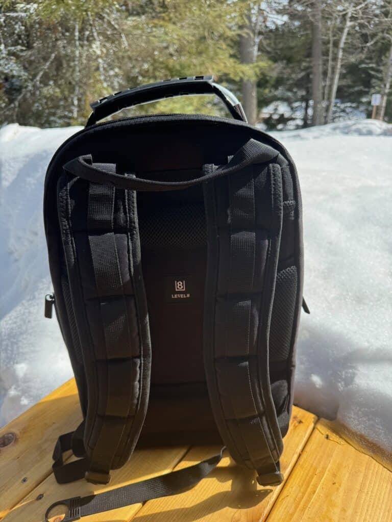 Backside of black backpack sitting on cedar decking against a snowbank