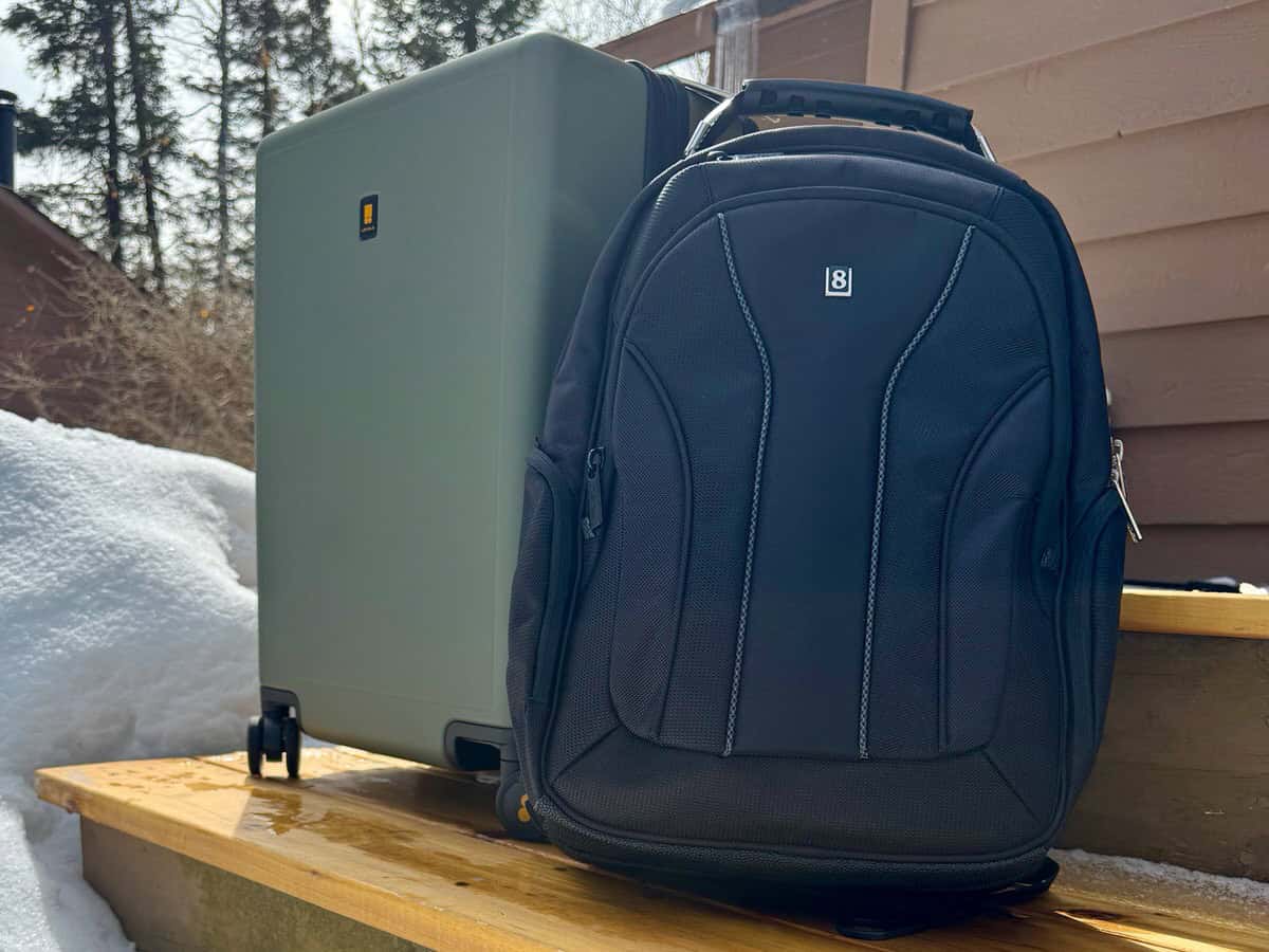 A green roller suitcase and a black backpack sit on an outside step