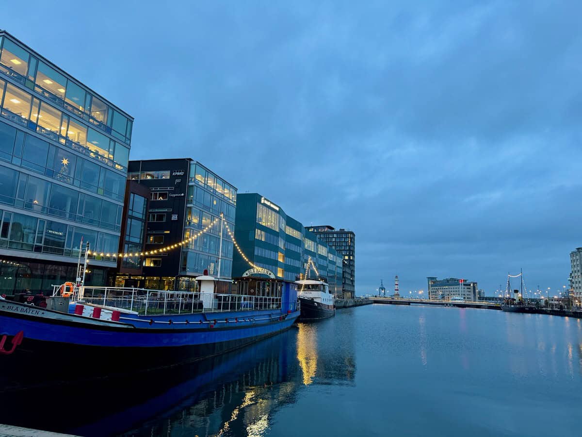 A boat with Christmas lights docked in the Malmo harbor near downtown. The old lighthouse is in the distance.
