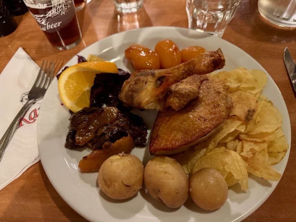 Dinner plate filled with roast duck, boiled potatoes, beets, cabbage, and potato chips.