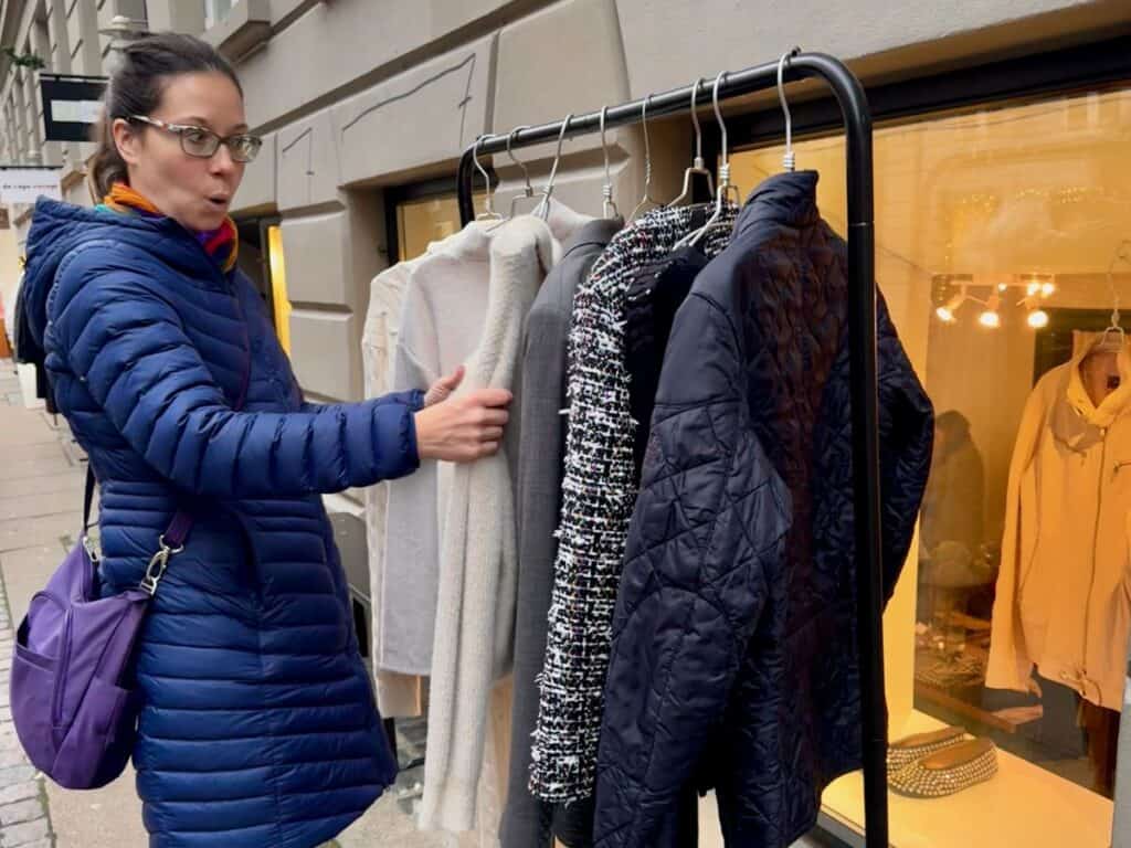 Woman exclaims over a find on an outdoor clothing rack filled with secondhand jackets