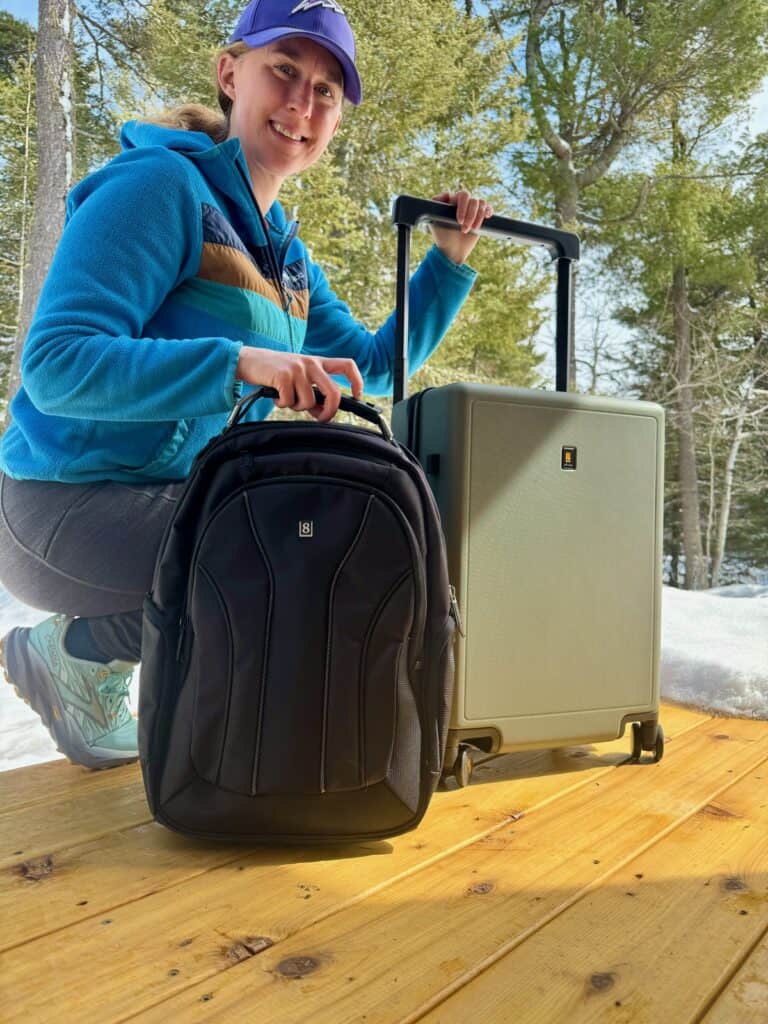 Crouching woman holds out a black laptop backpack and carry-on suitcase from LEVEL8 Luggage