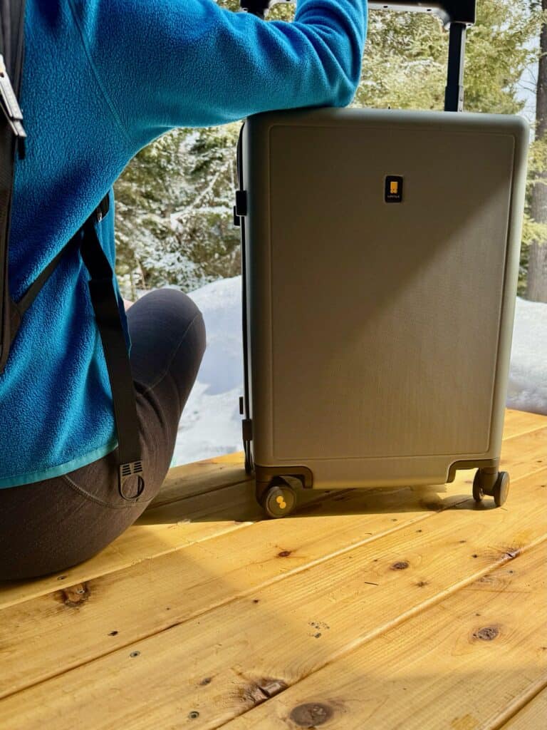 Woman sits next to a green LEVEL8 Voyageur suitcase
