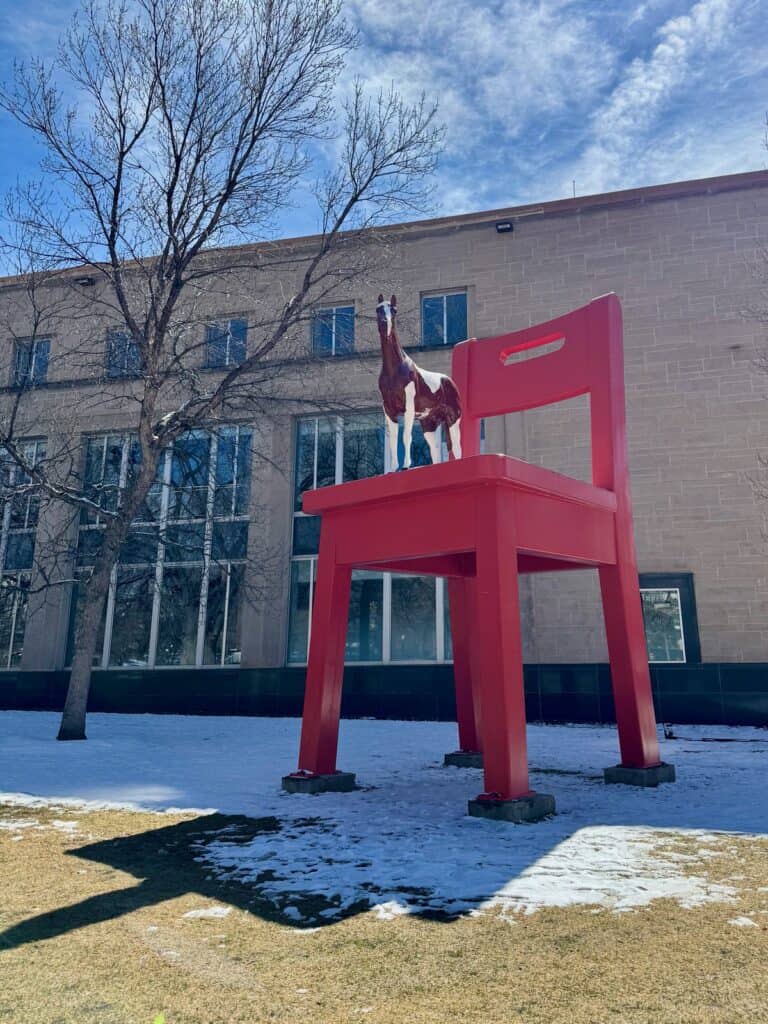 Sculpture of a brown and white horse on an oversized red chair outside the main branch of the Denver Public Library.