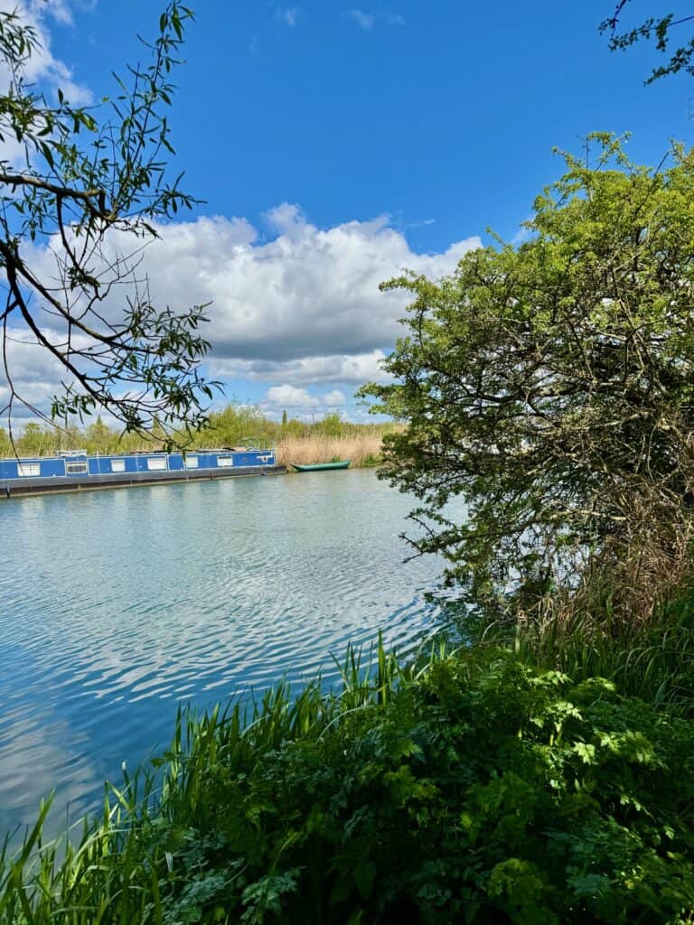 A houseboat and canoe float in the Thames on a sunny spring day