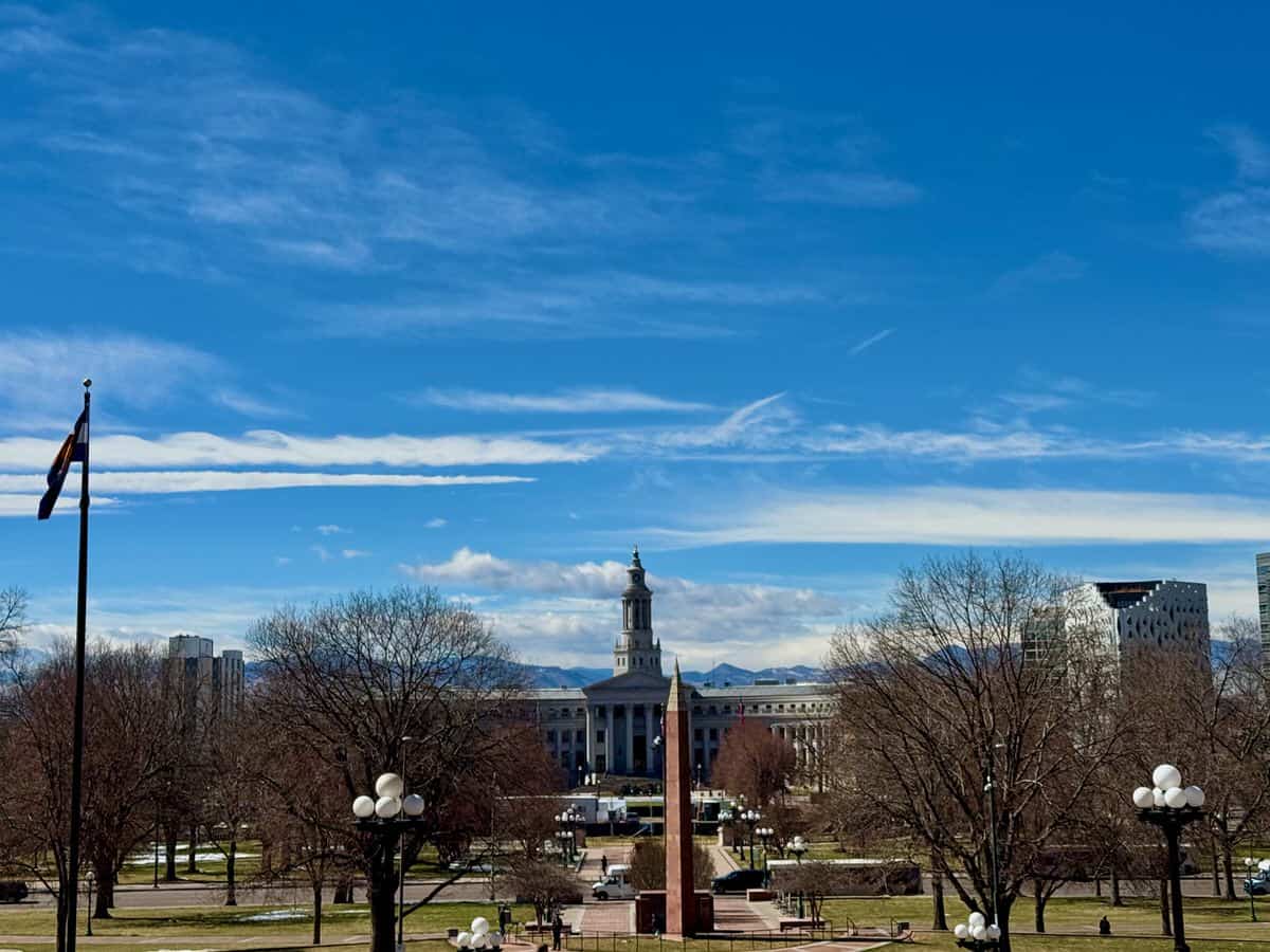 View of Denver City and County Building looking across Civic Center Park with the Rocky Mountains in the background.