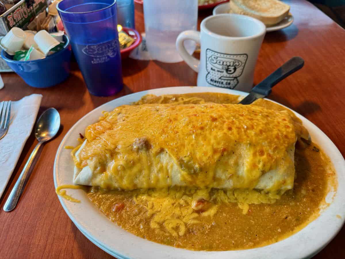 A large burrito covered with green chili sauce and melted cheese