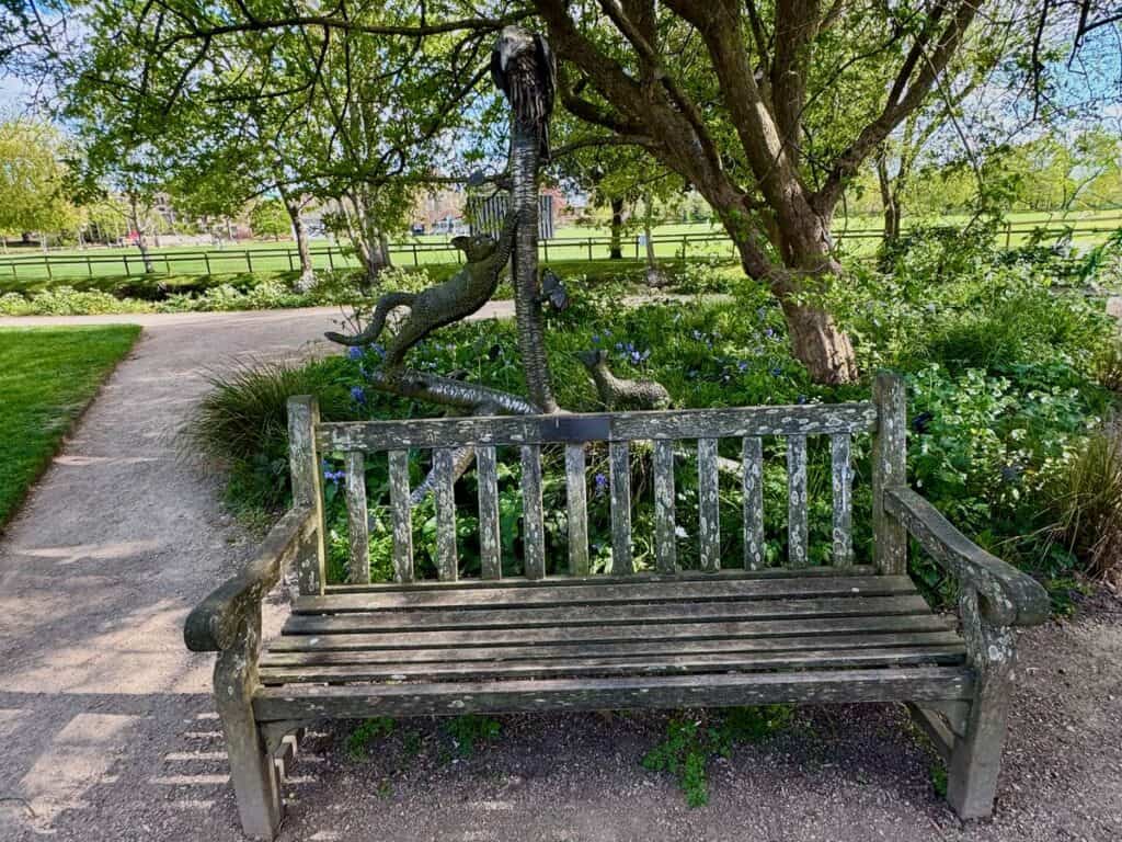 Park bench in botanic garden with a statue featuring a cat, polecat, and raven behind it.
